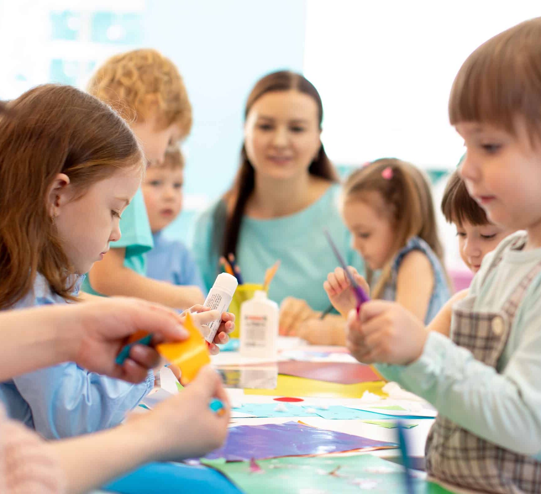 young girls around table painting with teacher watching