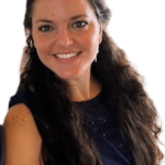 Smiling woman with long, dark curly hair wearing a navy blue sleeveless dress, posing against a light background.