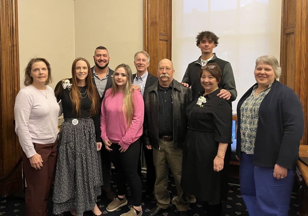 Nine people posing together indoors, dressed in semi-formal attire, smiling at the camera.