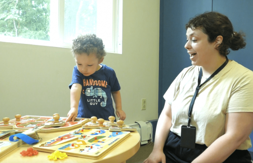 Young boy playing toys with teacher watching and encouraging