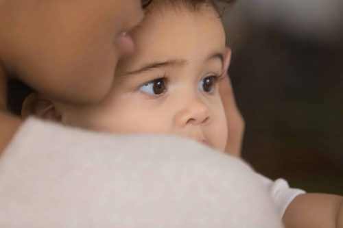 Close-up of a baby being held closely by an adult, showing the baby’s thoughtful expression.